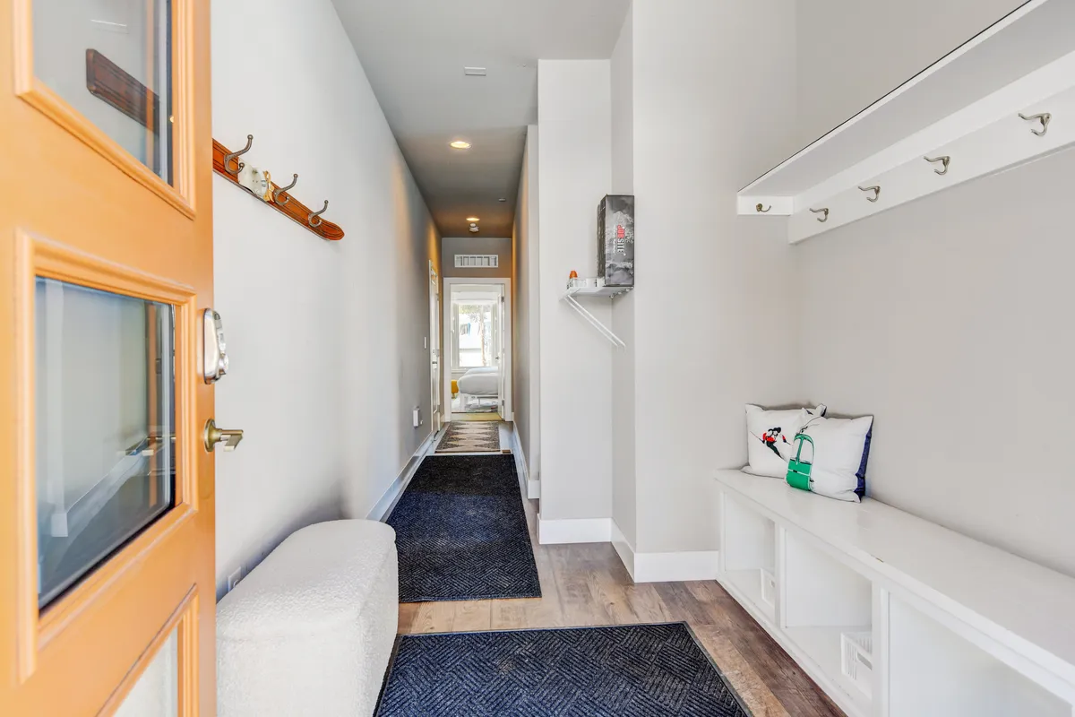 A bright and organized entryway with a modern front door, bench seating, coat hooks, and a runner rug. The space is designed for easy access, storage, and a welcoming first impression as guests step inside.