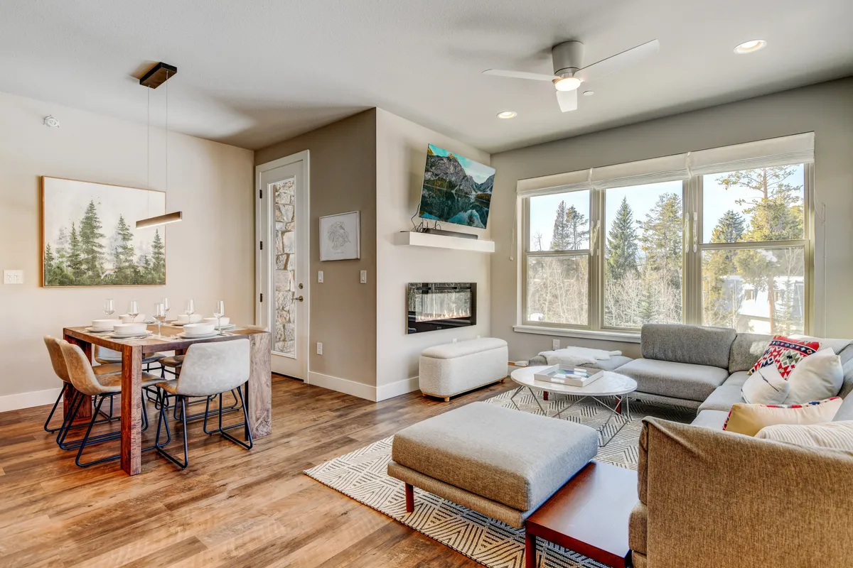 An open-concept space that features a dining table, a comfortable sofa, a striking fireplace, and large windows with natural light. Artwork adds a stylish touch, and the area is arranged for both dining and relaxation.