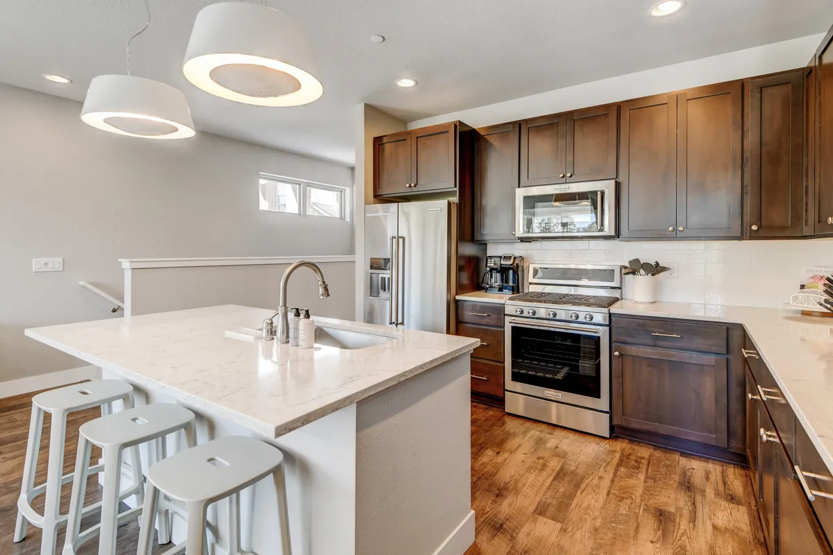 A cozy, modern kitchen scene with a central kitchen island, gleaming stainless steel appliances, and warm wooden cabinetry. The inviting setting hints at relaxed meals, celebrations, and shared moments around the island, with a clear view of the kitchen’s premium features.