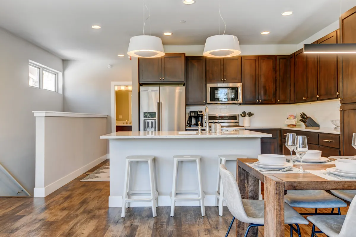 A spacious, light-filled room highlighting both a large kitchen island and a generously sized dining table, with elegant light fixtures overhead. The setup suggests effortless transitions between cooking and dining, with seating adaptable for both intimate dinners and festive group feasts.