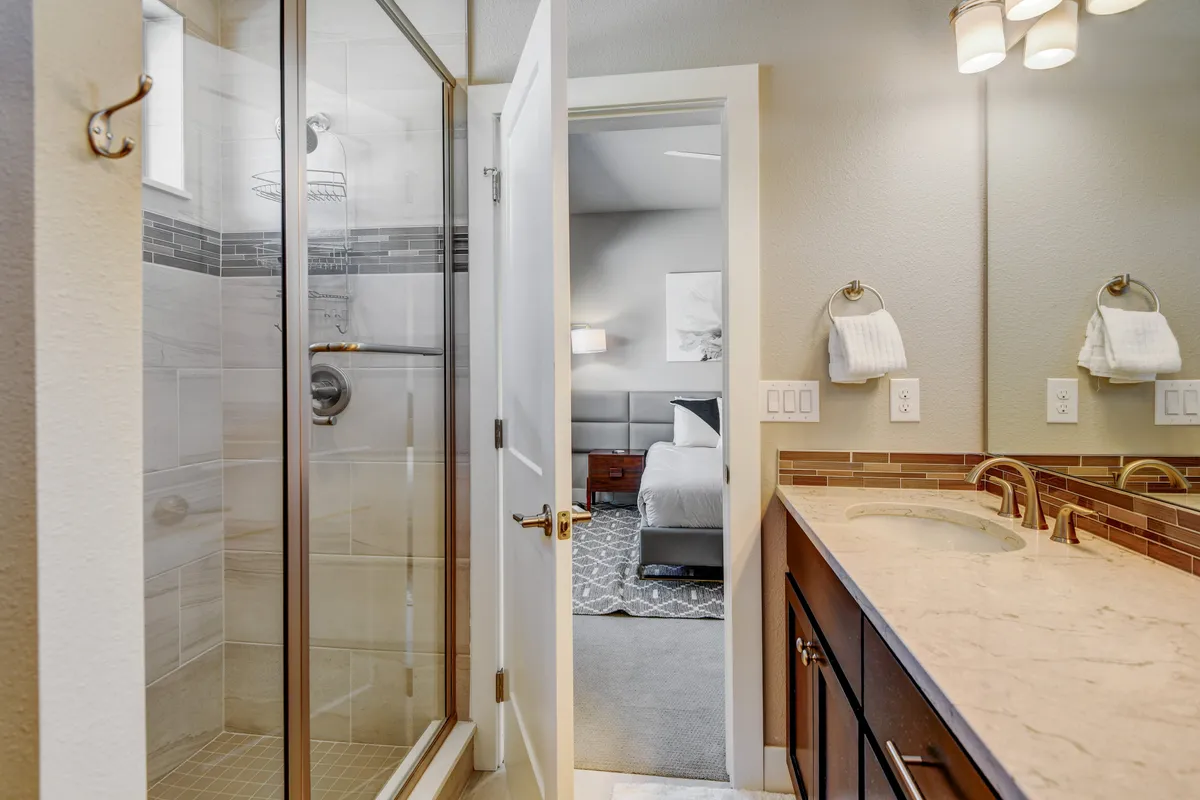 A modern ensuite bathroom with a glass shower enclosure, double vanity, and sleek fixtures. The space is bright and inviting, offering an upscale, spa-like experience for guests. Clean lines and organized surfaces emphasize comfort and relaxation.