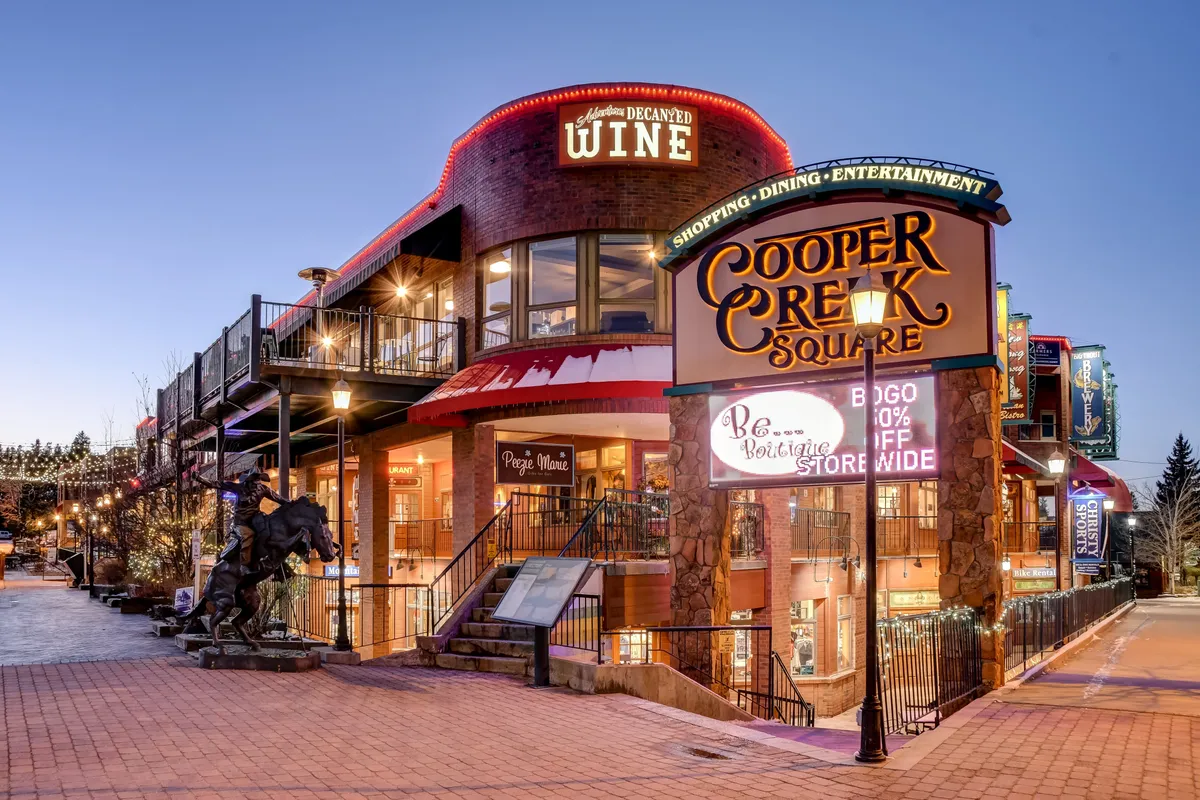 An exterior shot featuring the Cooper Creek Square sign, wine shop signage, outdoor seating, and a horse sculpture. The area is lively, signaling a vibrant downtown atmosphere ideal for shopping, dining, and nightlife.