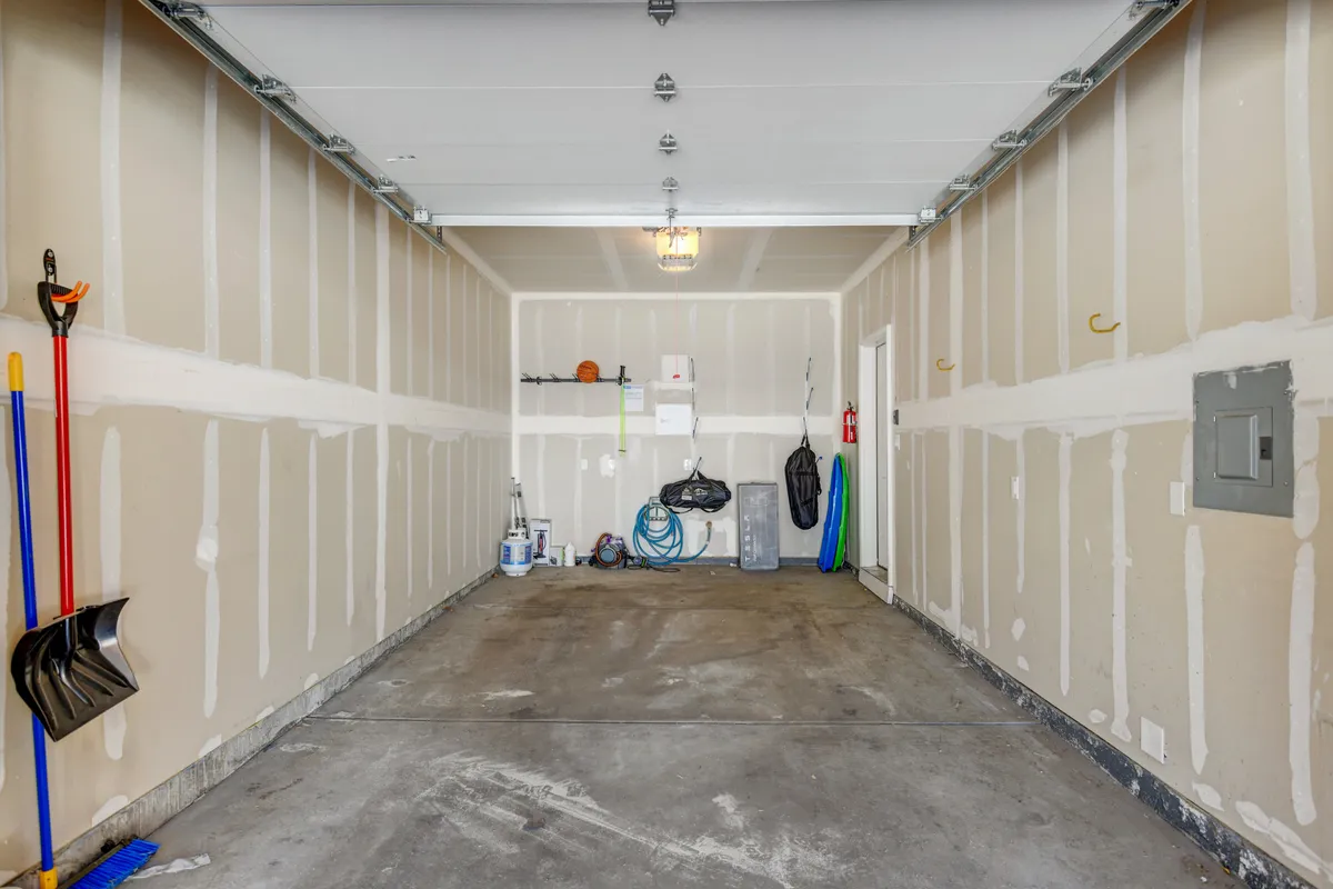 This interior view of the garage shows a clean concrete floor, a visible garage door, utility shelves, and storage tools, making it perfect for parking, storing bikes, or keeping adventure gear organized.