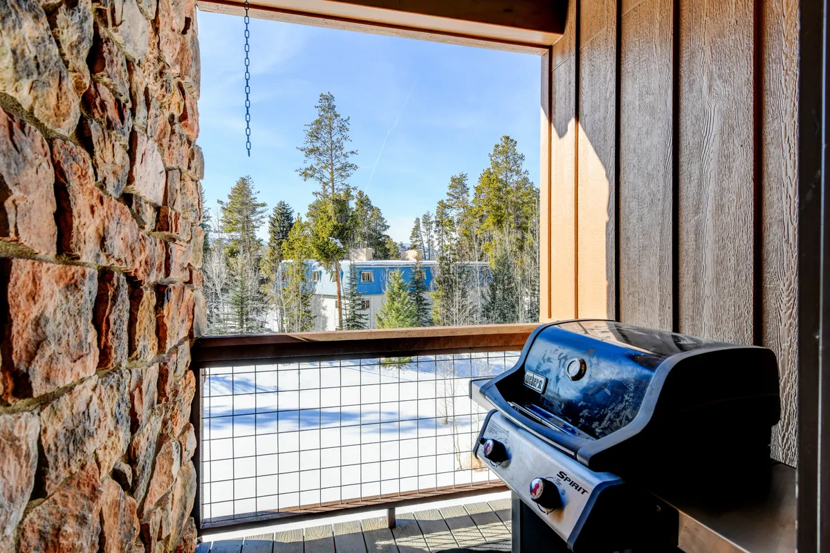 An exterior shot of the patio with a grill, framed by a window and surrounded by a snowy landscape and pine trees. The setup is ideal for outdoor relaxation and casual gatherings, with the comfort of the patio just steps away from nature.